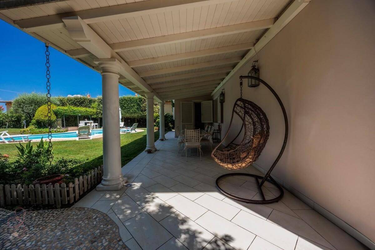 Überdachte Terrasse mit Hängesessel und Blick auf den Garten und den Swimmingpool.
