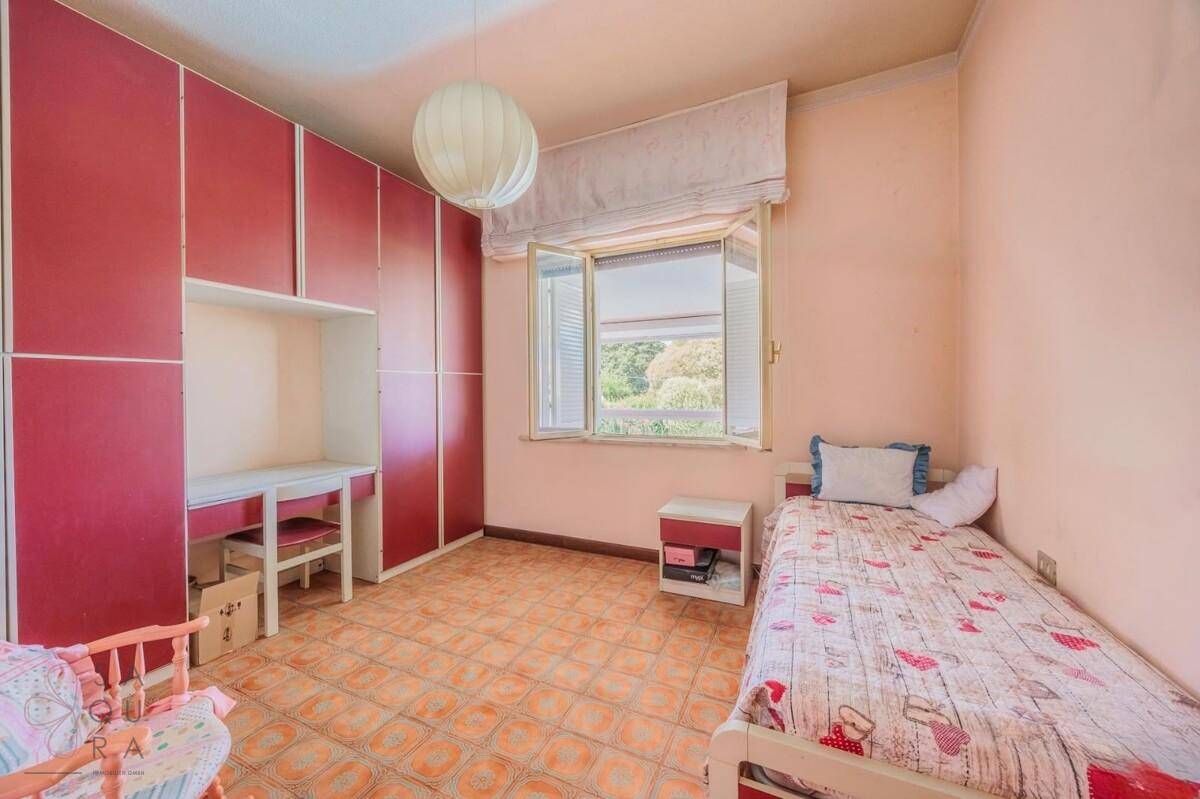Kinderzimmer mit Terrakotta-Fliesenboden, roten Einbauschränken und einem Einzelbett.
