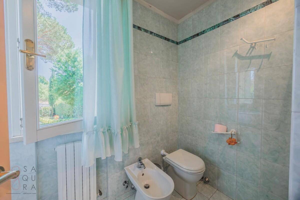 Helles Badezimmer mit hellgrünen Fliesen, Toilette, Bidet und einem Fenster mit Blick ins Grüne.