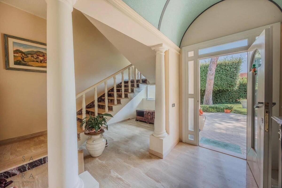 Heller Eingangsbereich mit Marmorboden, eleganter Treppe und Zugang zum Garten.