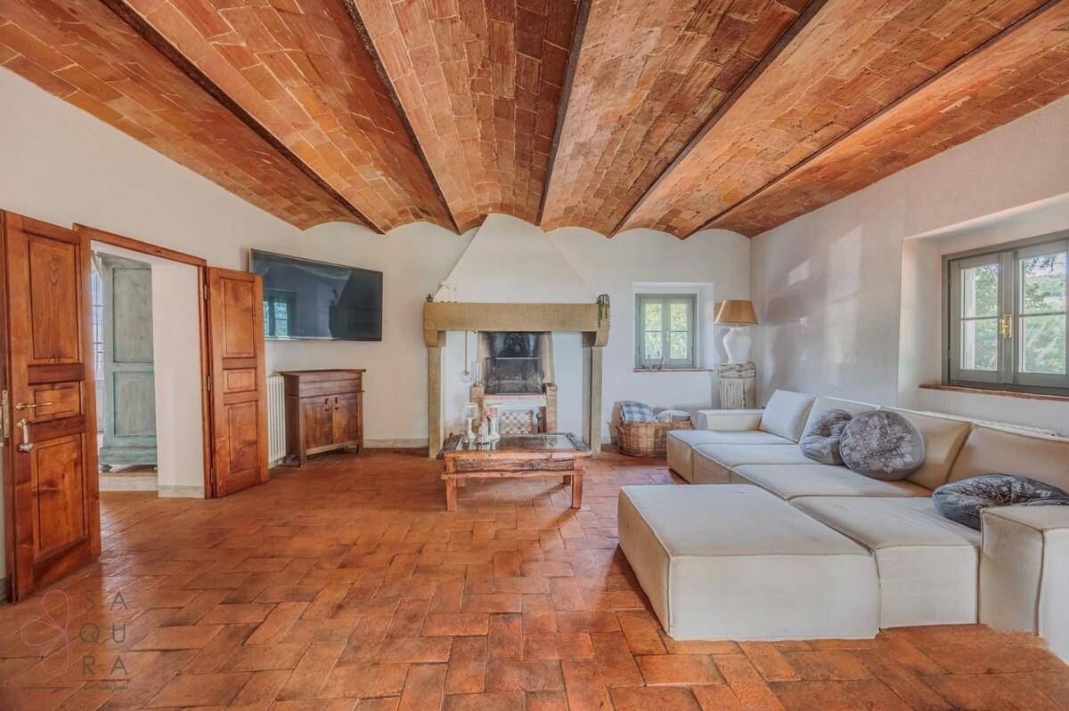 Geräumiges Wohnzimmer mit Terrakottaboden, freiliegenden Ziegeldecken und einem traditionellen Kamin.