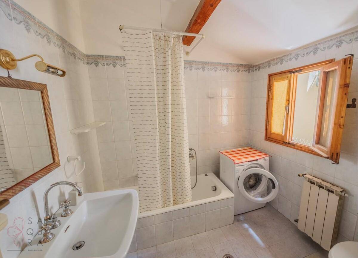 Badezimmer mit Badewanne, Waschmaschine und Fenster für Tageslicht.