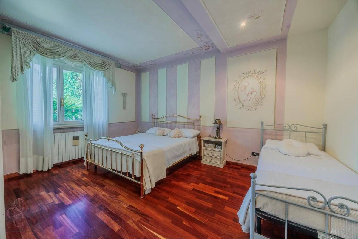 Helles Schlafzimmer mit Holzboden, zwei Betten und einer dekorativen Decke in Pastelltönen.