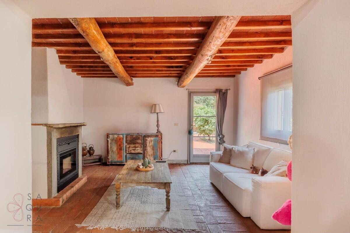 Gemütliches Wohnzimmer mit Kamin, Holzbalkendecke und Zugang zum Garten durch eine Glastür.