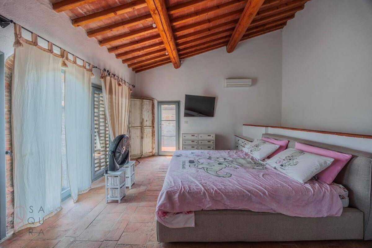 Schlafzimmer mit Terrakottaboden, Holzbalkendecke, Klimaanlage und Zugang zu einem Balkon.