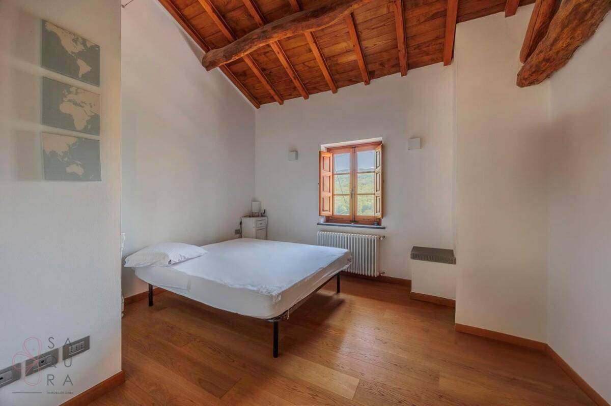 Schlafzimmer mit Holzbalkendecke, Holzboden und einem Fenster mit Blick ins Grüne.