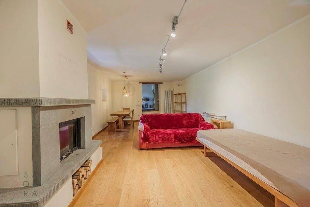 Heller Wohn- und Essbereich mit Kamin, Holzfußboden und rotem Sofa.