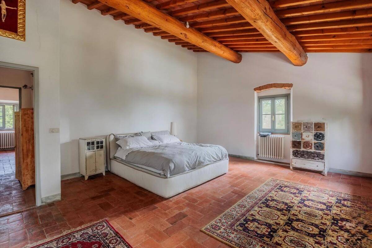 Großes Schlafzimmer mit Terrakottaboden, Holzbalkendecke und traditionellen Teppichen.