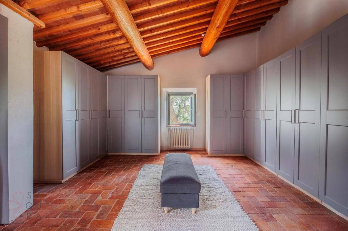 Geräumiges Ankleidezimmer mit Einbauschränken, Terrakottaboden und Holzbalkendecke.