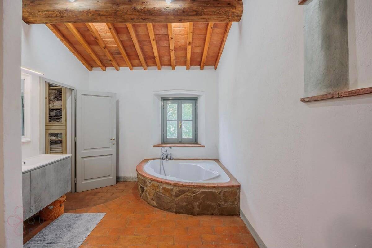 Badezimmer mit Eckbadewanne, Terrakottaboden und Holzbalkendecke.