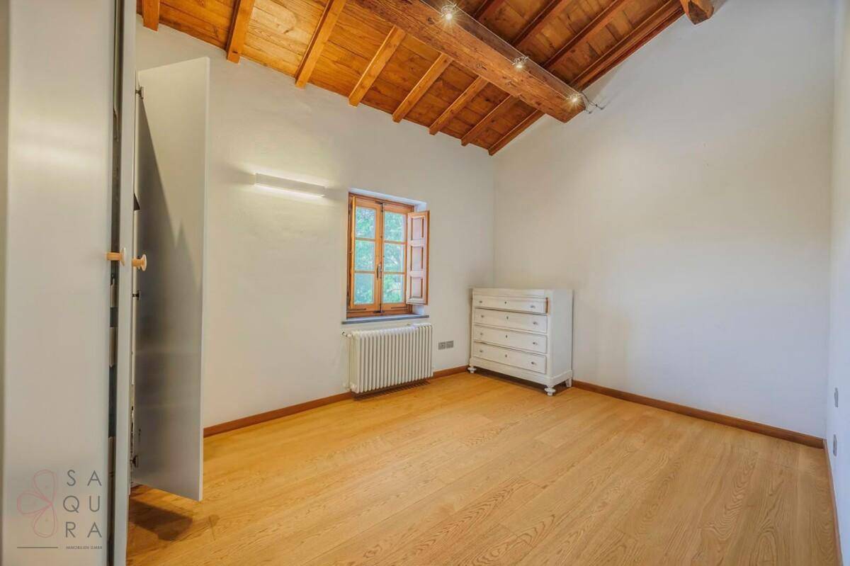 Helles Schlafzimmer mit Holzbalkendecke, Holzboden und einer Kommode.