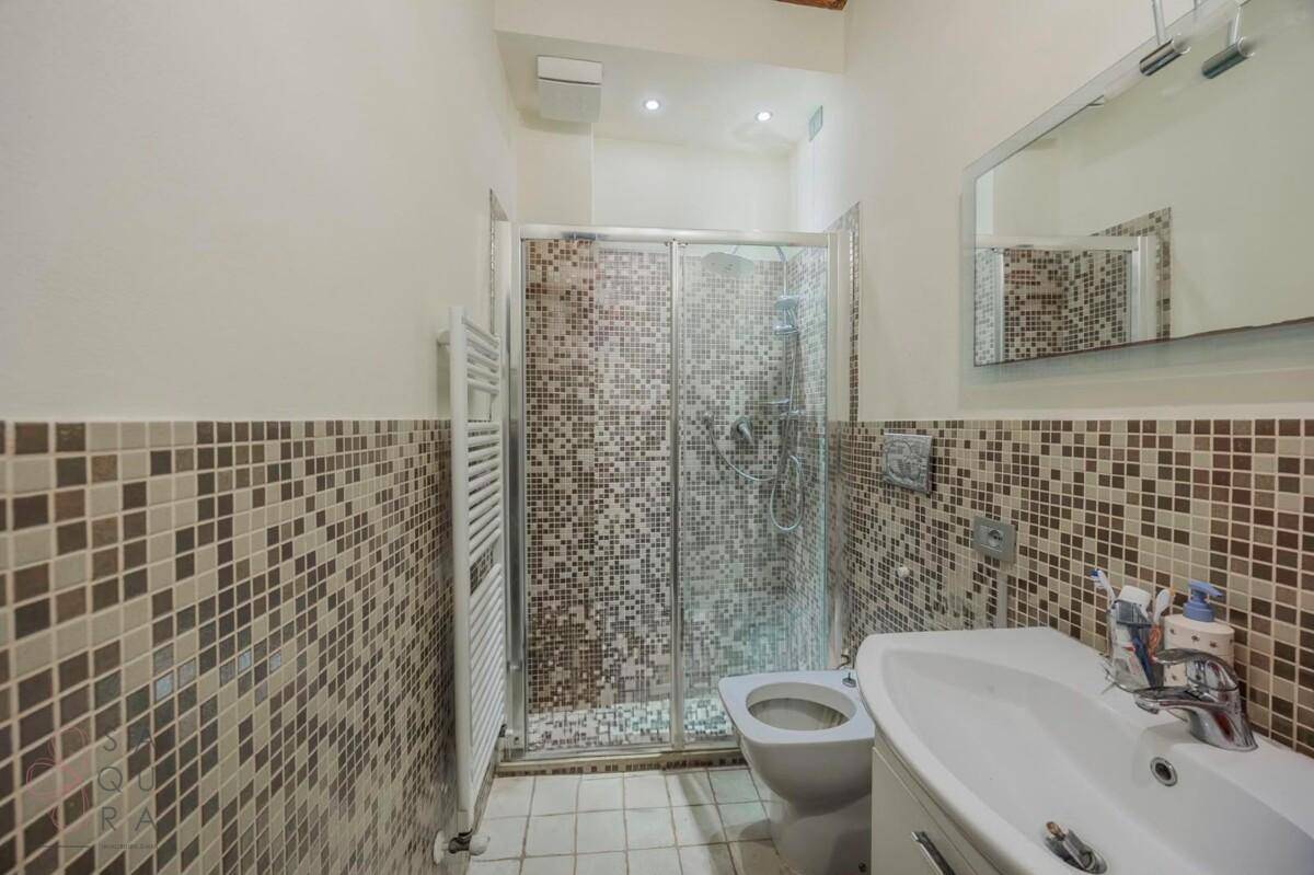Modernes Badezimmer mit Mosaikfliesen, Duschkabine und beheiztem Handtuchhalter.