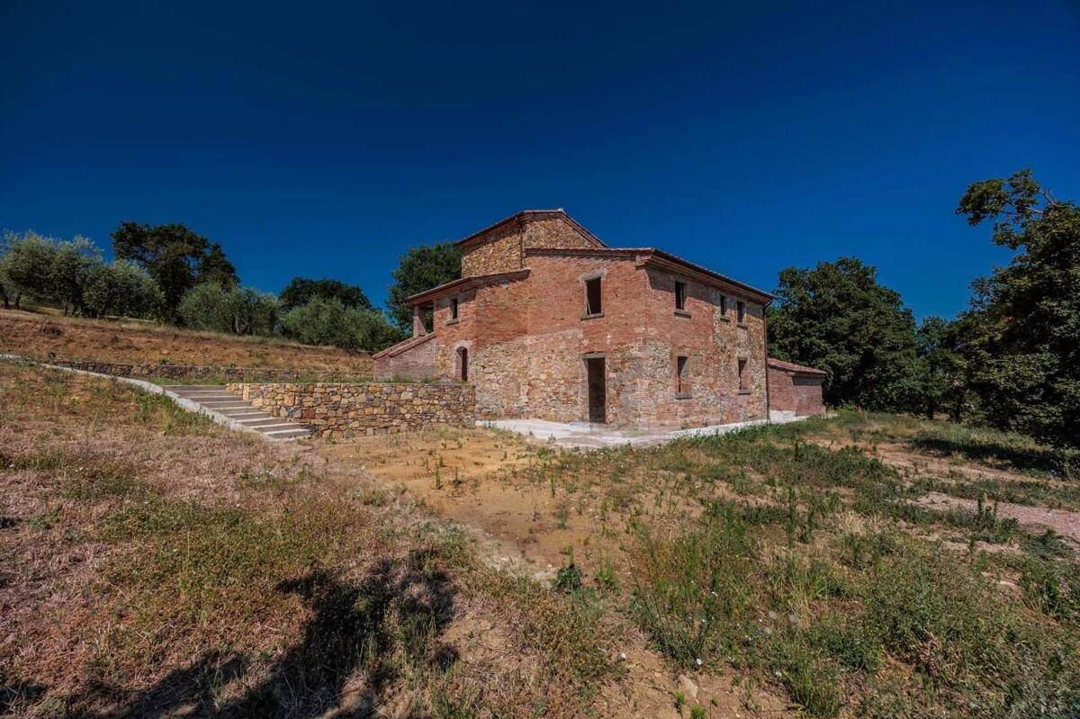 Rustikales Landhaus mit Steinfassade und Ziegeldach, umgeben von mediterraner Vegetation unter blauem Himmel.