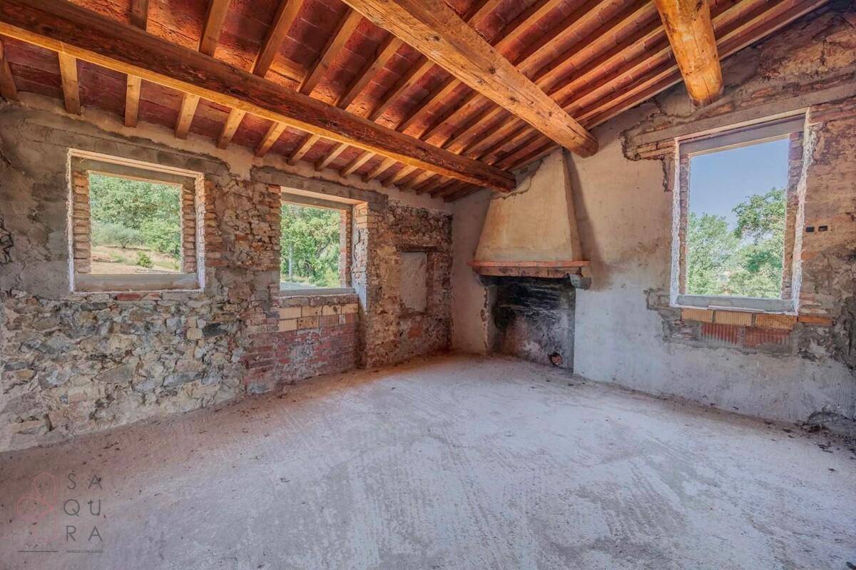 Unfertiger Innenraum mit freiliegenden Holzbalken, Steinwänden und einem traditionellen Kamin.