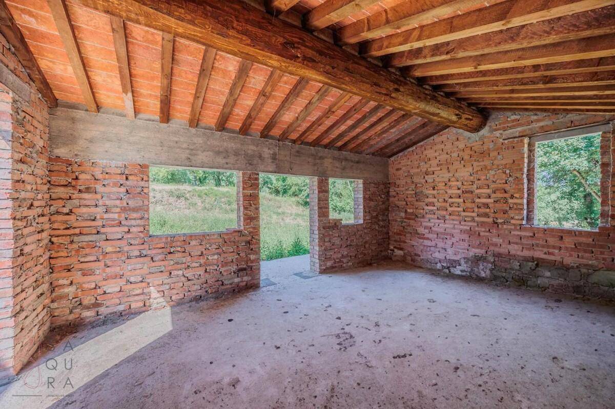 Rohbau eines Raumes mit Ziegelwänden und Holzbalkendecke, große Fensteröffnungen bieten viel Licht.