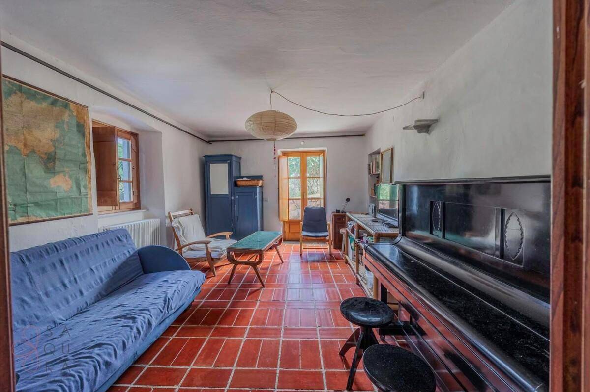 Rustikales Wohnzimmer mit Terrakottaboden, blauem Sofa und Klavier, strahlt gemütliche Atmosphäre aus.
