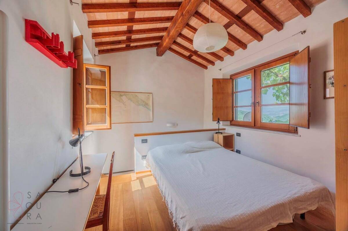 Helles Schlafzimmer mit Holzbalkendecke und Holzboden, bietet einen Arbeitsbereich und Ausblick.