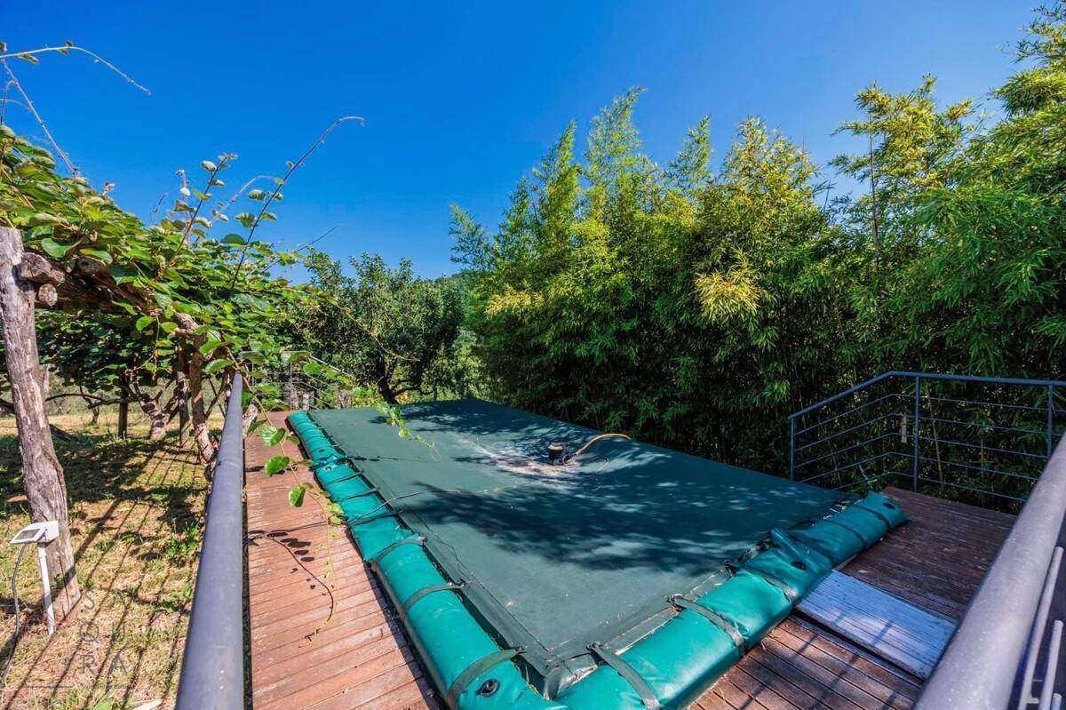 Abgedeckter Poolbereich auf einer Holzterrasse, umgeben von üppiger Vegetation und Bambusbäumen.