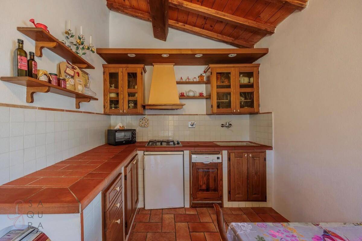 Kleine, funktionale Küche mit Terrakotta-Arbeitsplatten, Holzschränken und sichtbaren Deckenbalken.