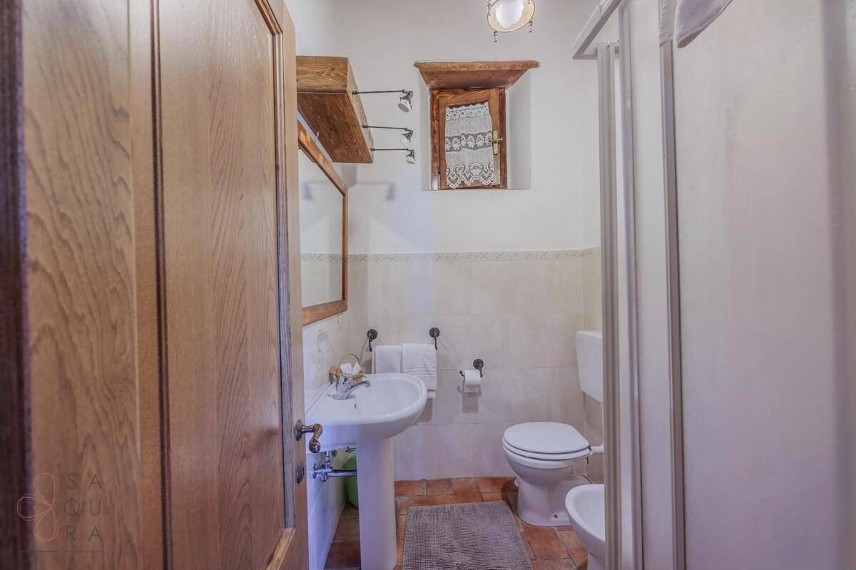 Kleines Badezimmer mit Dusche, Waschbecken, Toilette und Terrakotta-Boden.