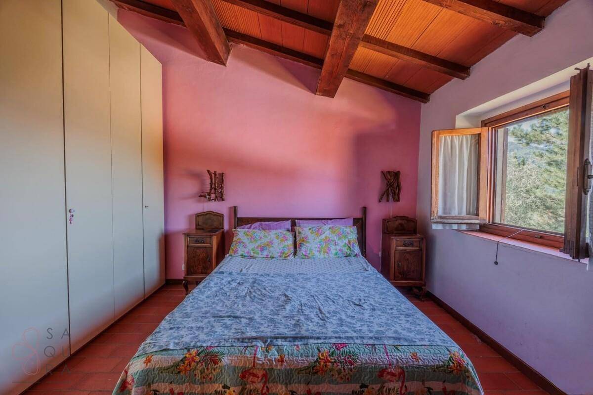 Schlafzimmer mit rosa Wänden, Doppelbett, Terrakotta-Boden und sichtbaren Holzbalken an der Decke.