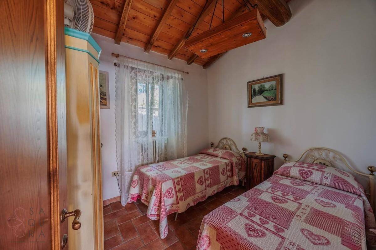 Helles Schlafzimmer mit zwei Einzelbetten, Terrakotta-Boden und rustikaler Holzbalkendecke.