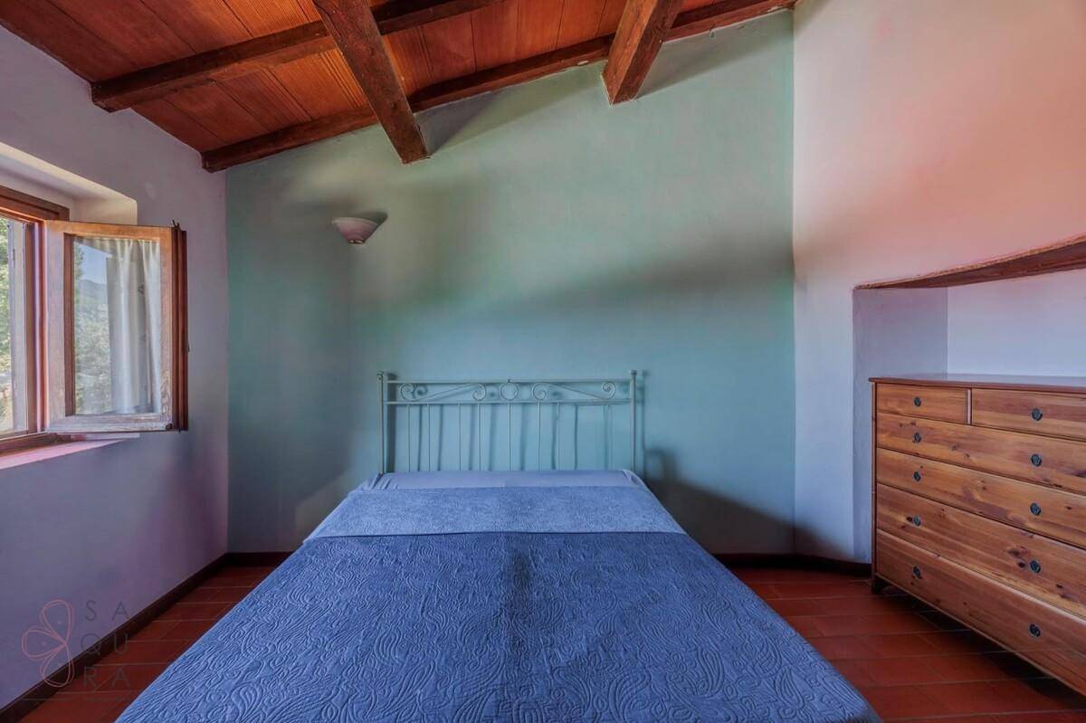 Schlafzimmer mit hellgrünen Wänden, Einzelbett, Terrakotta-Boden und rustikaler Holzbalkendecke.