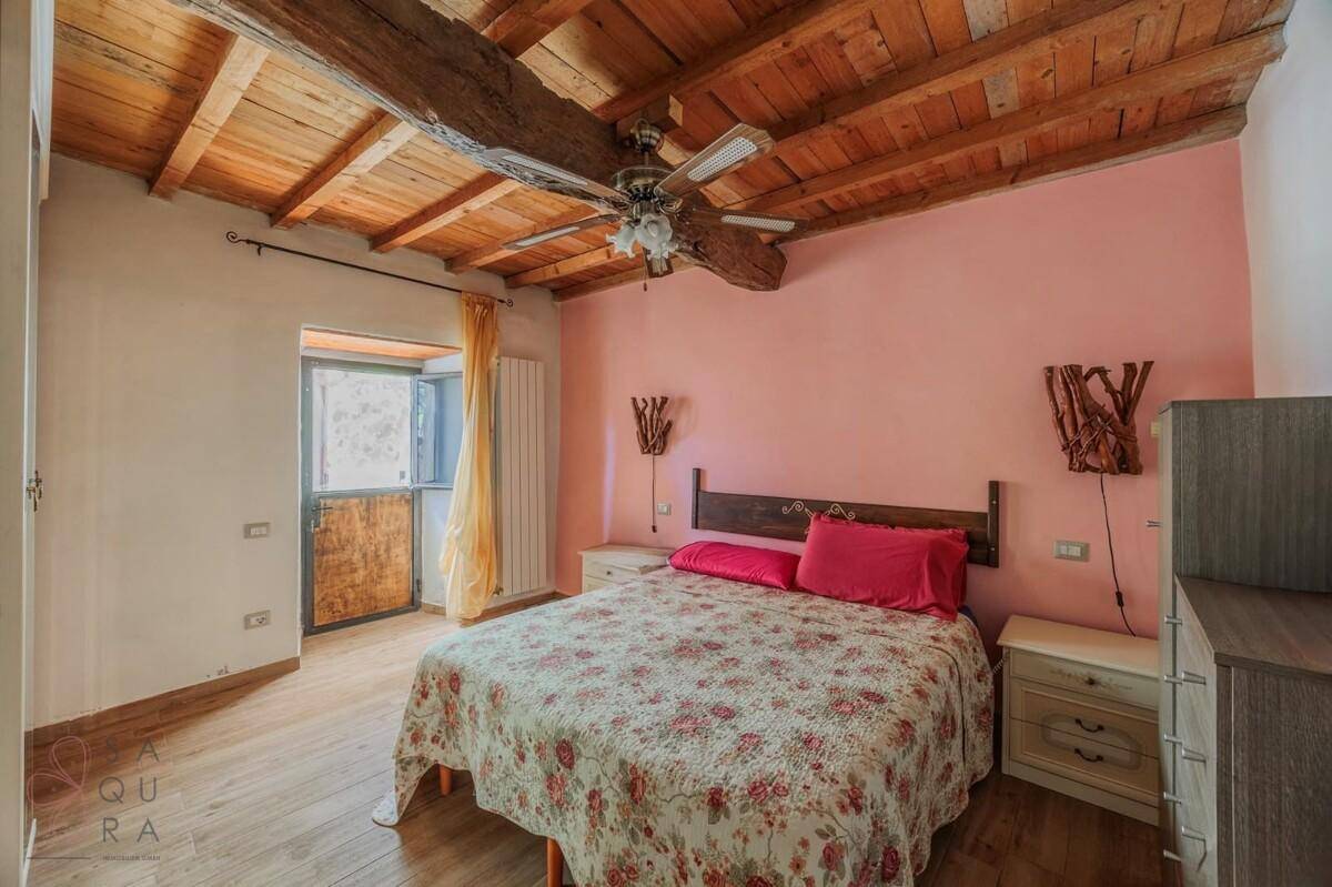 Schlafzimmer mit rosa Wänden, Doppelbett, Holzboden und sichtbaren Deckenbalken.