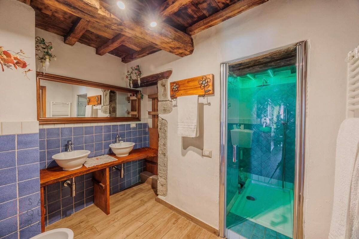 Badezimmer mit blauen Fliesen, Doppelwaschbecken, Dusche und Holzbalkendecke.