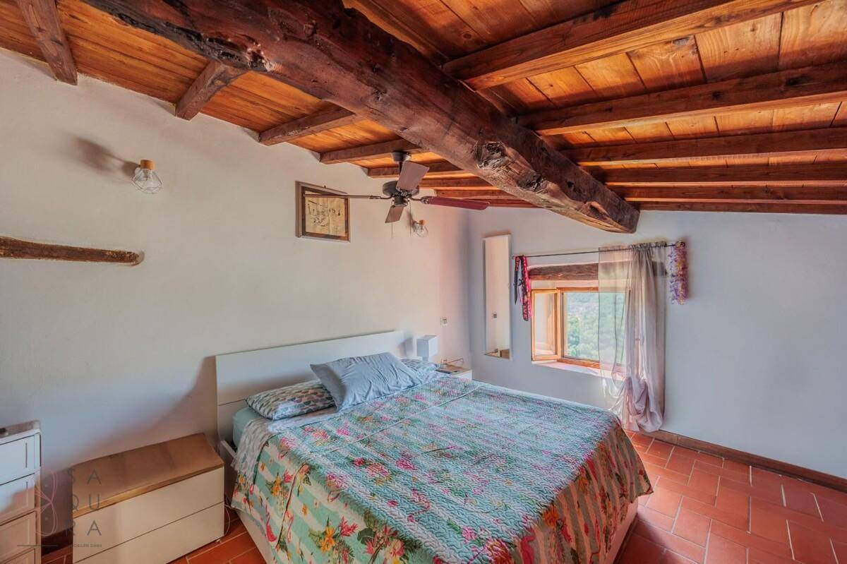 Schlafzimmer mit Doppelbett, Terrakotta-Boden, Holzbalkendecke und Deckenventilator.