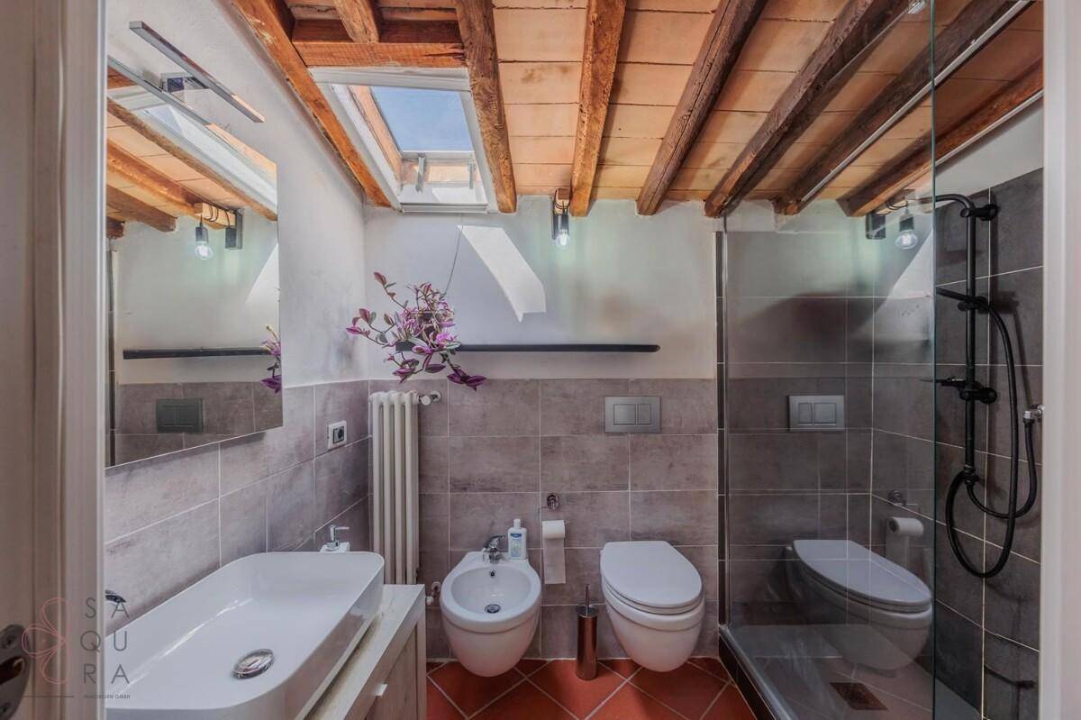 Modernes Badezimmer mit Dusche, Bidet, Hänge-WC, grauen Fliesen und Dachfenster.