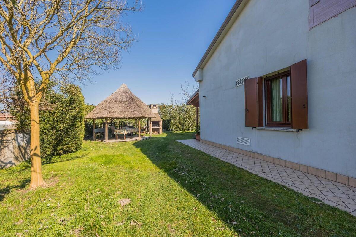Grüner Gartenbereich mit einem strohgedeckten Pavillon und einem gemauerten Grillplatz für gesellige Stunden.