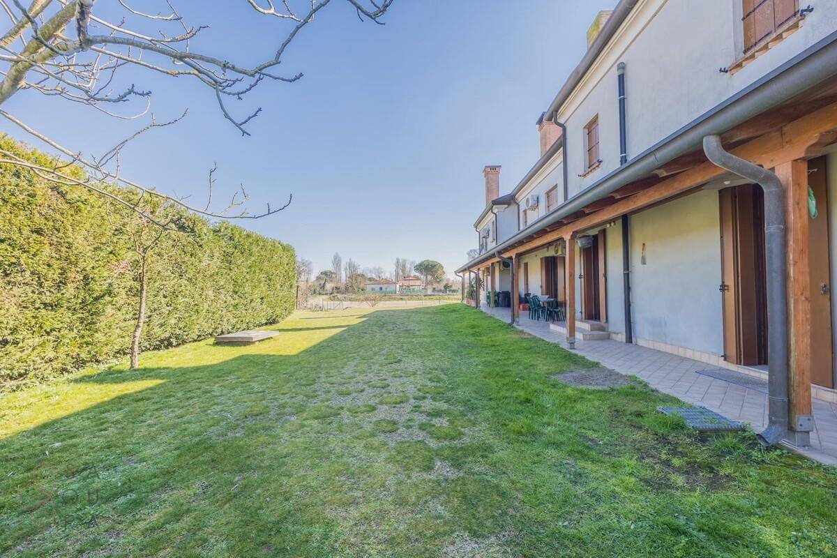 Lange überdachte Terrasse entlang der Hausrückseite mit Blick auf den weitläufigen grünen Rasen.