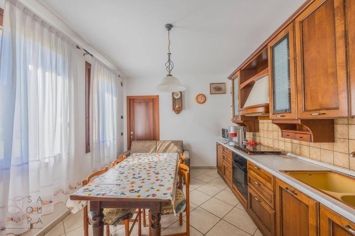 Traditionelle Wohnküche mit Holzschränken, Essbereich und Blick nach draußen durch große Fenster.