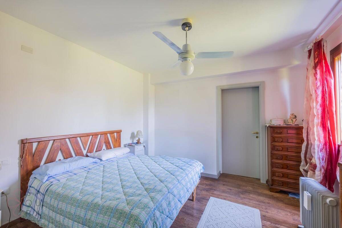 Schlafzimmer mit Holzbett, Deckenventilator und Fenster mit roten Vorhängen.