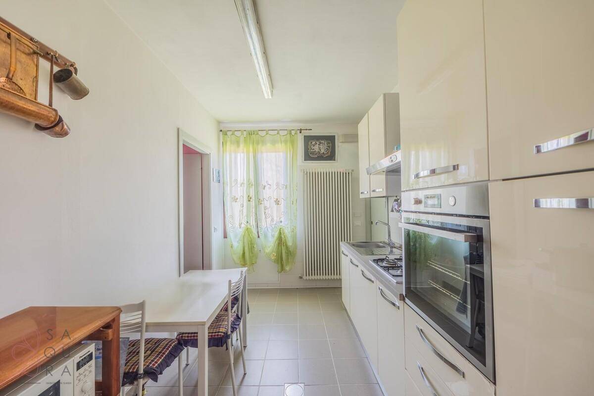 Moderne, helle Küche mit weißen Hochglanzschränken, integriertem Backofen und Essbereich am Fenster.