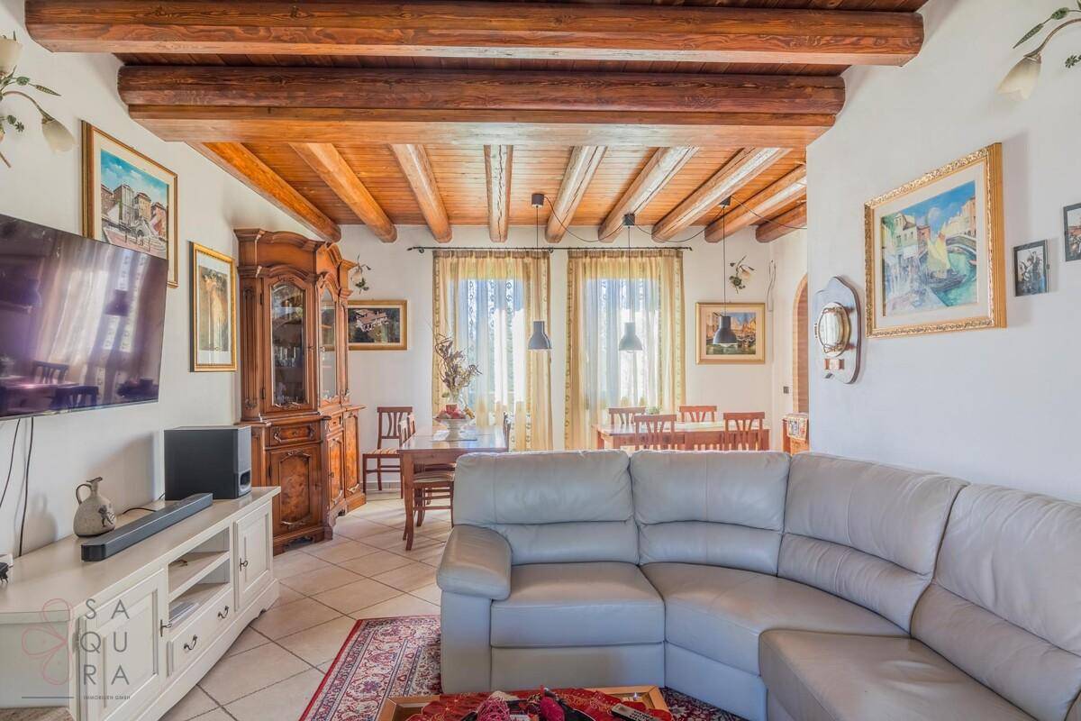 Geräumiges Wohnzimmer mit bequemer Couch, Holzbalkendecke und Blick auf den Essbereich im Hintergrund.