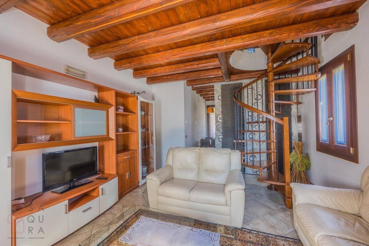 Wohnzimmer mit Holzbalkendecke, gemütlicher Sitzecke und einer eleganten Wendeltreppe.