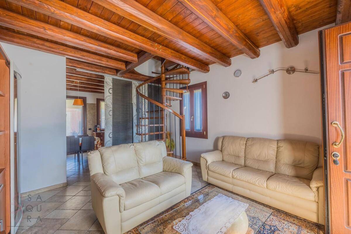 Gemütliches Wohnzimmer mit Holzbalkendecke, beigen Sofas und einer eleganten Wendeltreppe.