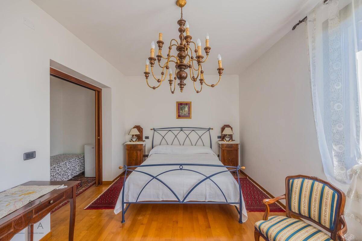 Schlafzimmer mit Holzboden, schmiedeeisernem Bett und traditionellem Kronleuchter.