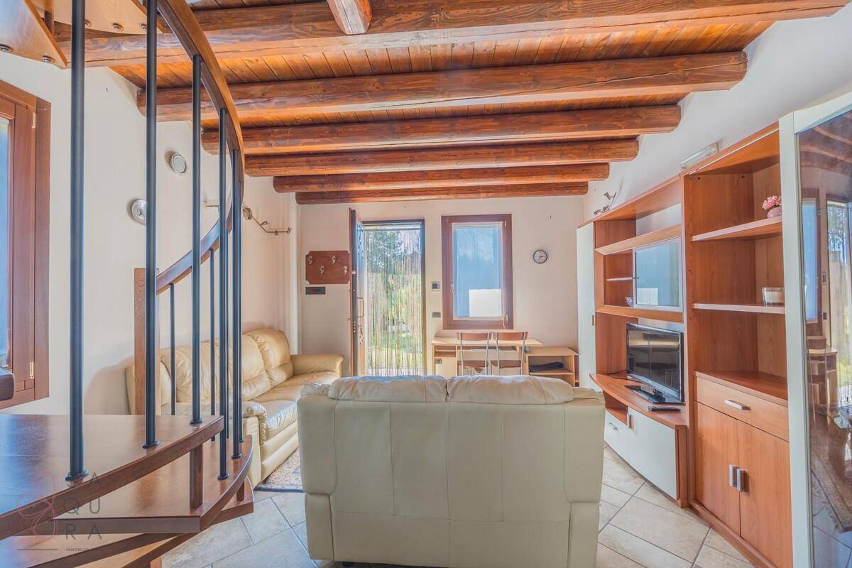 Helles Wohnzimmer mit Holzbalkendecke, beigen Sofas und Blick in den Garten.