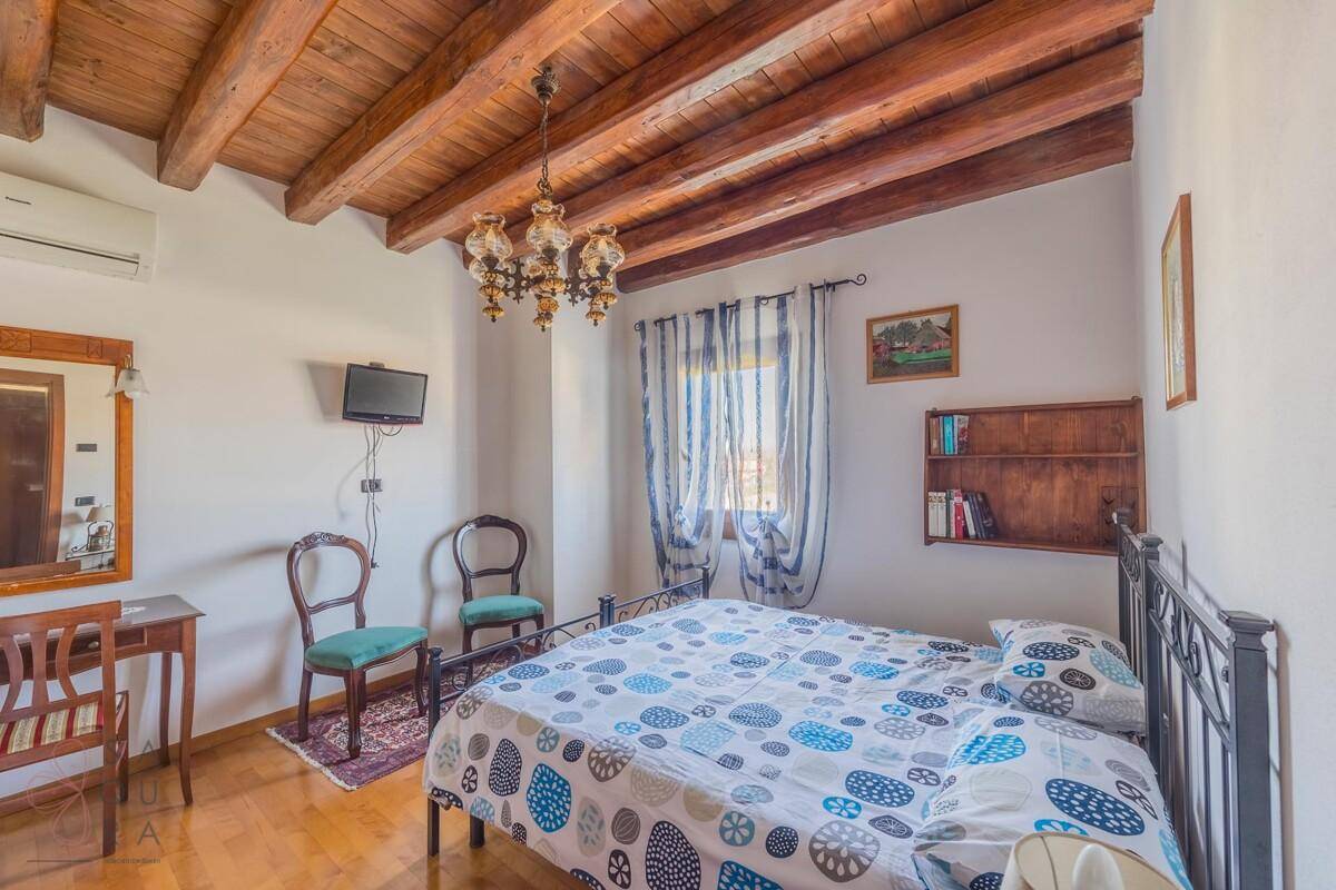Schlafzimmer mit Holzbalkendecke, schmiedeeisernem Bett und traditionellem Kronleuchter.