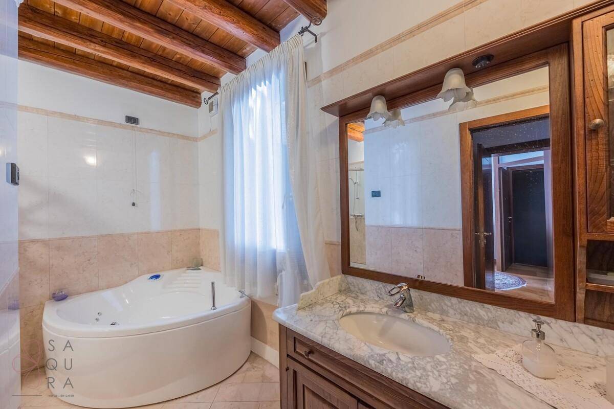 Geräumiges Badezimmer mit Eckbadewanne, Marmorwaschtisch und Holzbalkendecke.