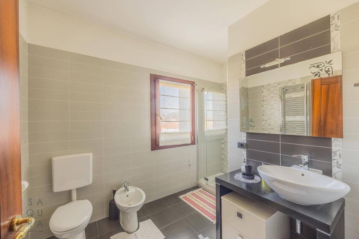 Modernes Badezimmer mit grauen Fliesen, WC, Bidet, Waschbecken und Duschkabine.