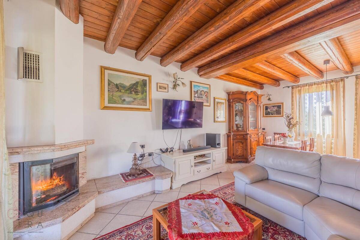 Helles Wohnzimmer mit Kamin, Holzbalkendecke und gemütlicher Sitzecke, ideal für entspannte Abende.