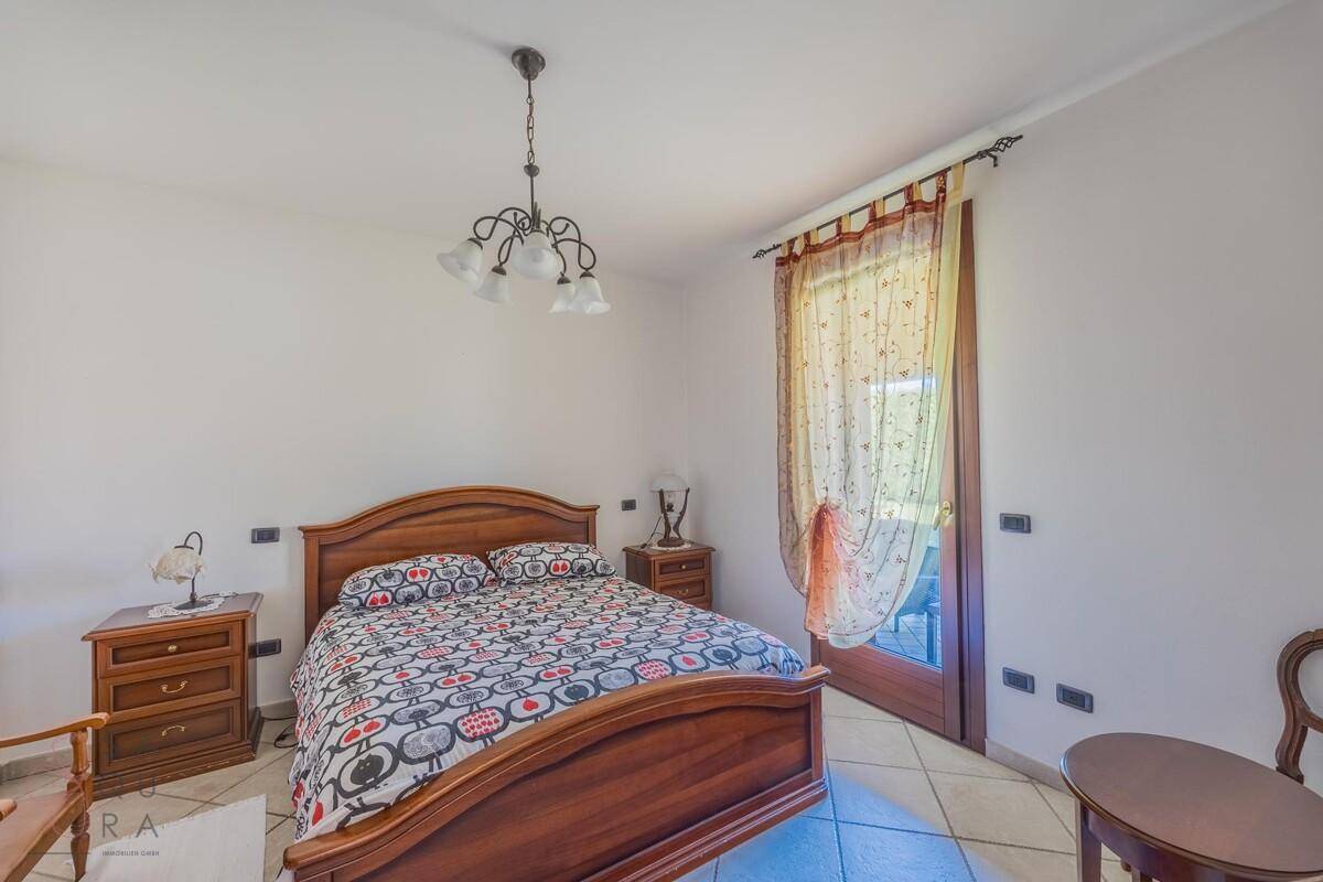 Schlafzimmer mit Holzbett, Nachttischen und Zugang zu einem Außenbereich.