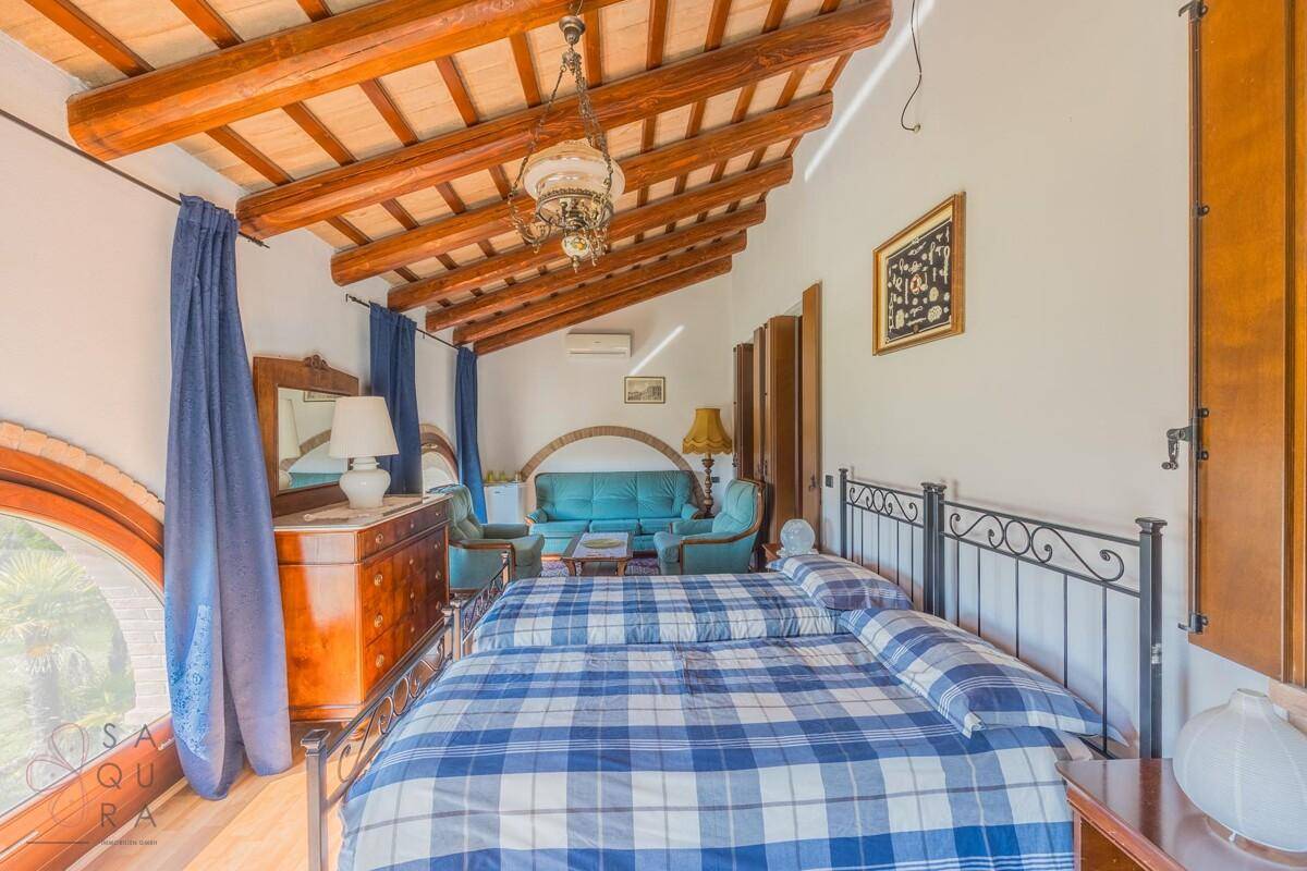 Helles Schlafzimmer mit Holzbalkendecke, zwei Betten und einem runden Fenster.