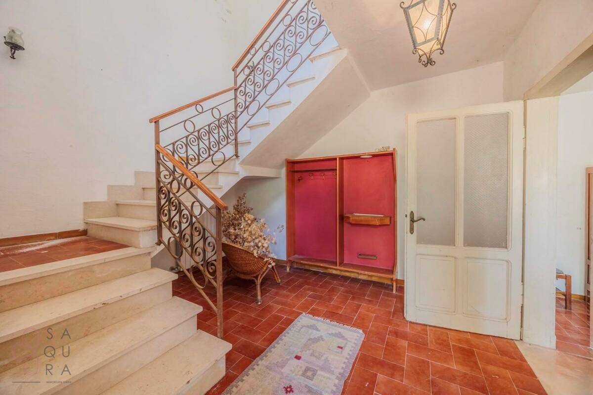 Eingangsbereich mit geschwungener Treppe, schmiedeeisernem Geländer und Terrakottafliesen.