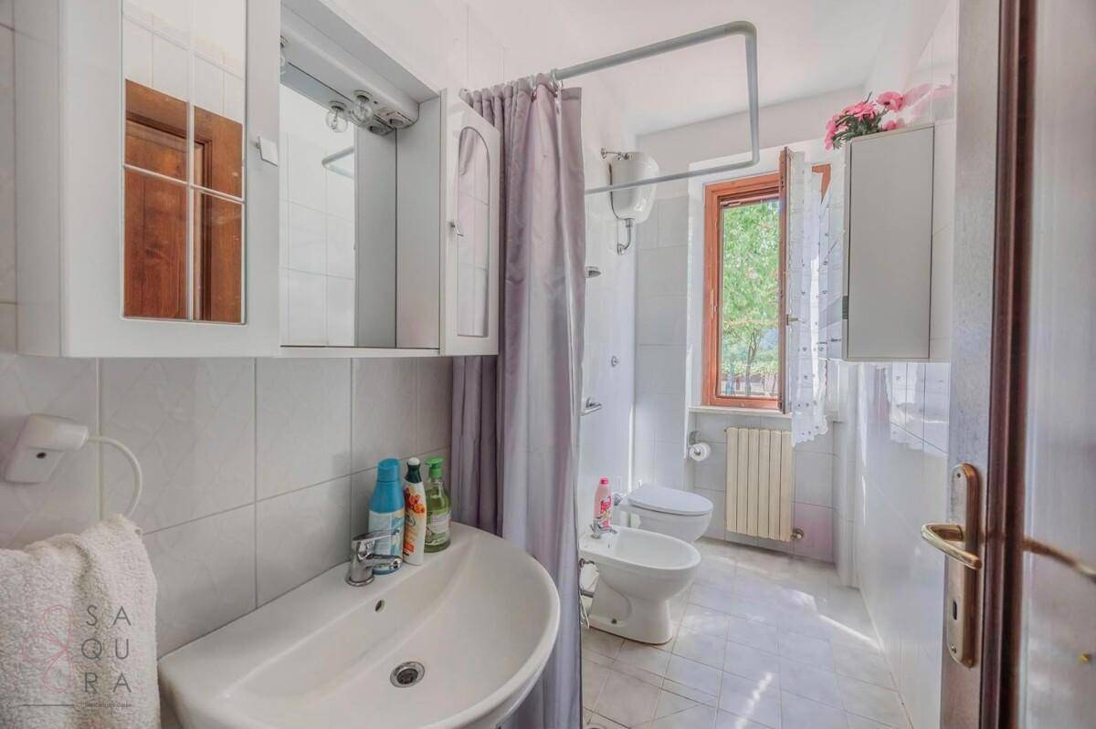 Helles Badezimmer mit weißen Fliesen, Waschbecken, Toilette, Bidet und Duschvorhang.