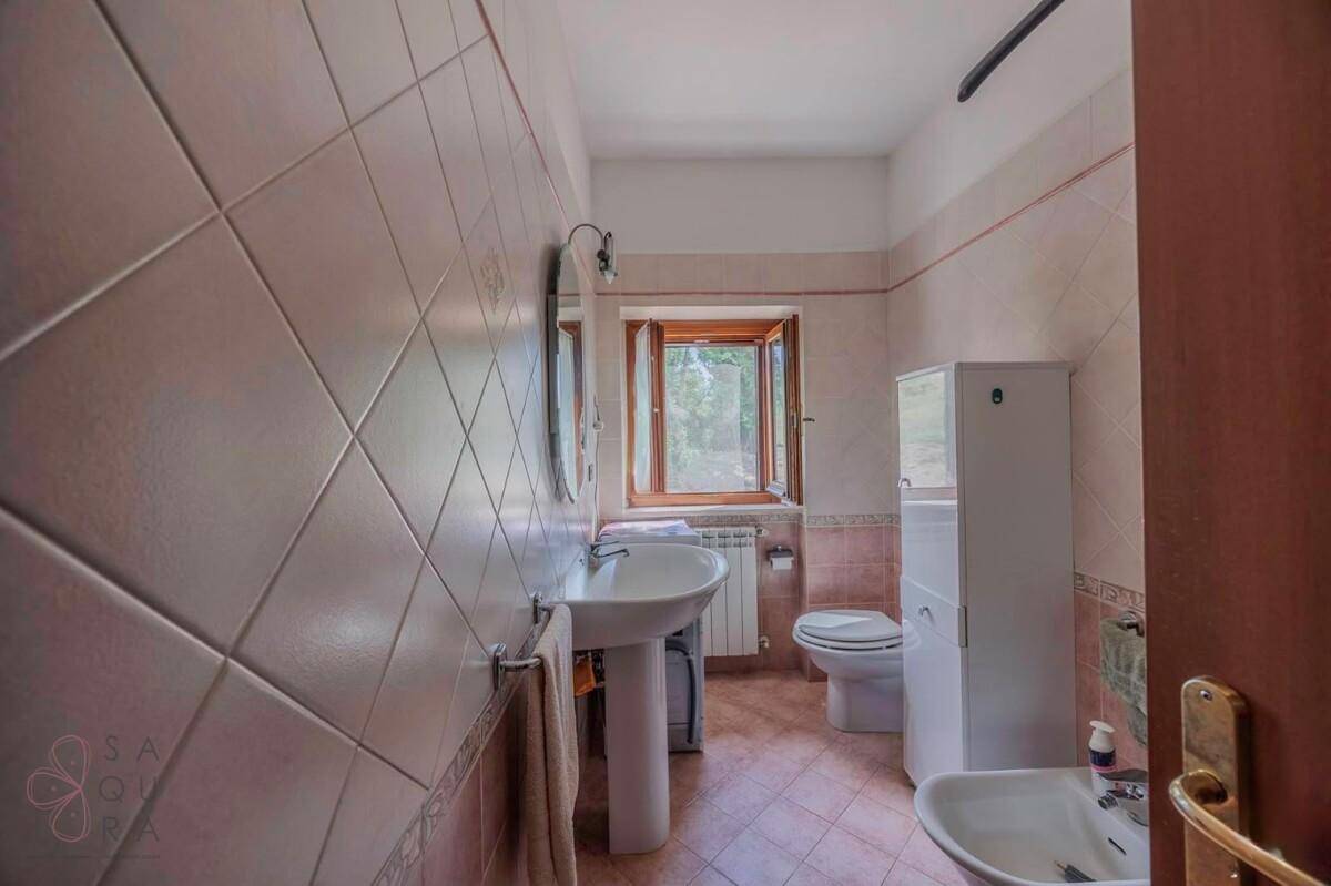 Badezimmer mit rosa Fliesen, Standwaschbecken, Toilette, Bidet und einem Fenster.